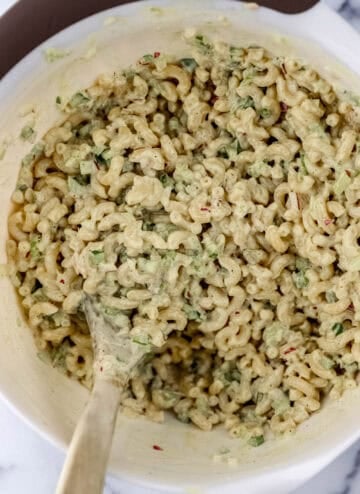 Macaroni salad ingredients combined in mixing bowl with wooden spoon.