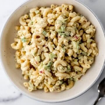 Overhead view of macaroni salad in white bowl by a spoon.