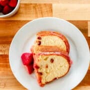 Overhead view of slices of cake on a white plate by bowl of strawberries.
