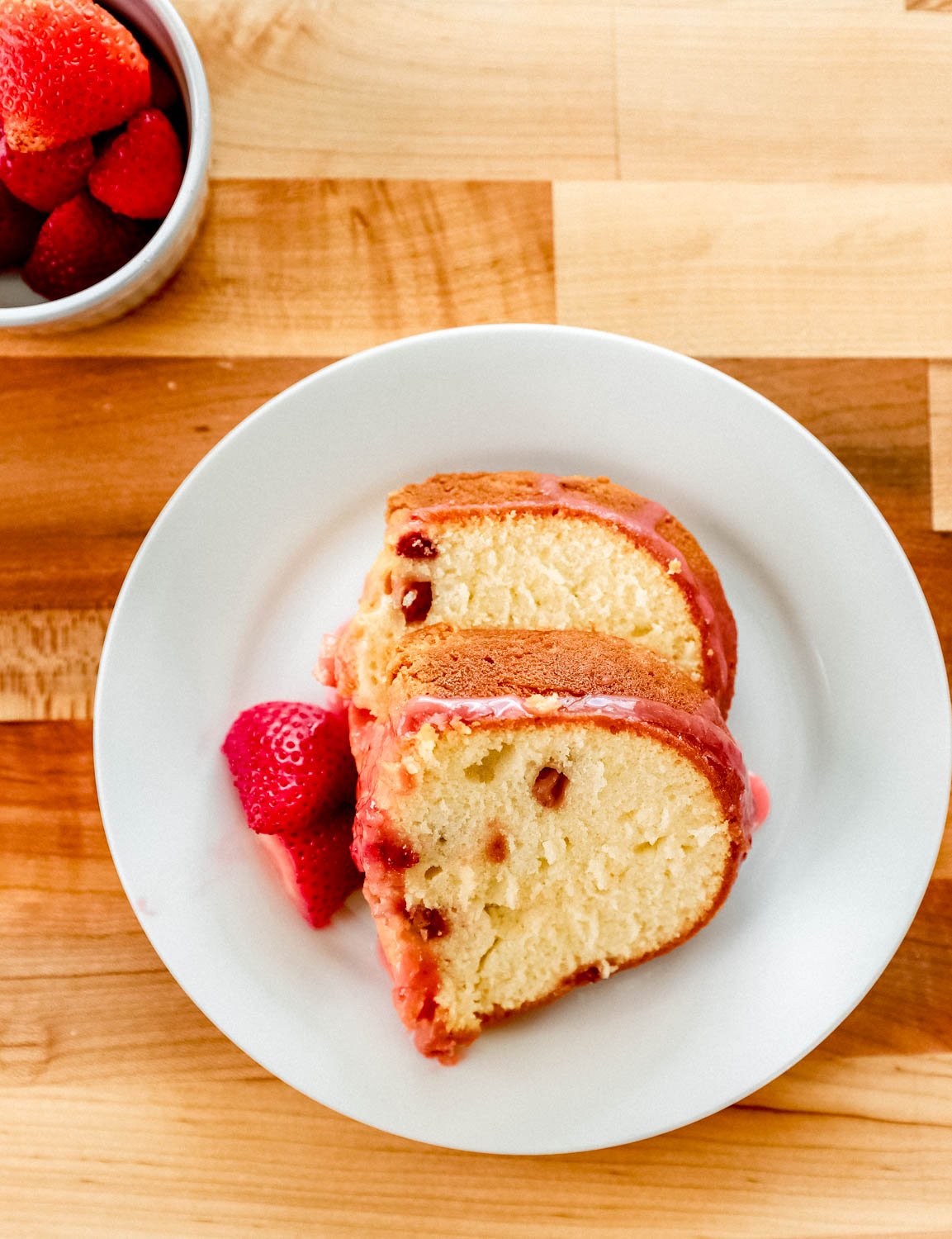 Overhead view of two slices of cake on white plate by bowl of strawberries. 