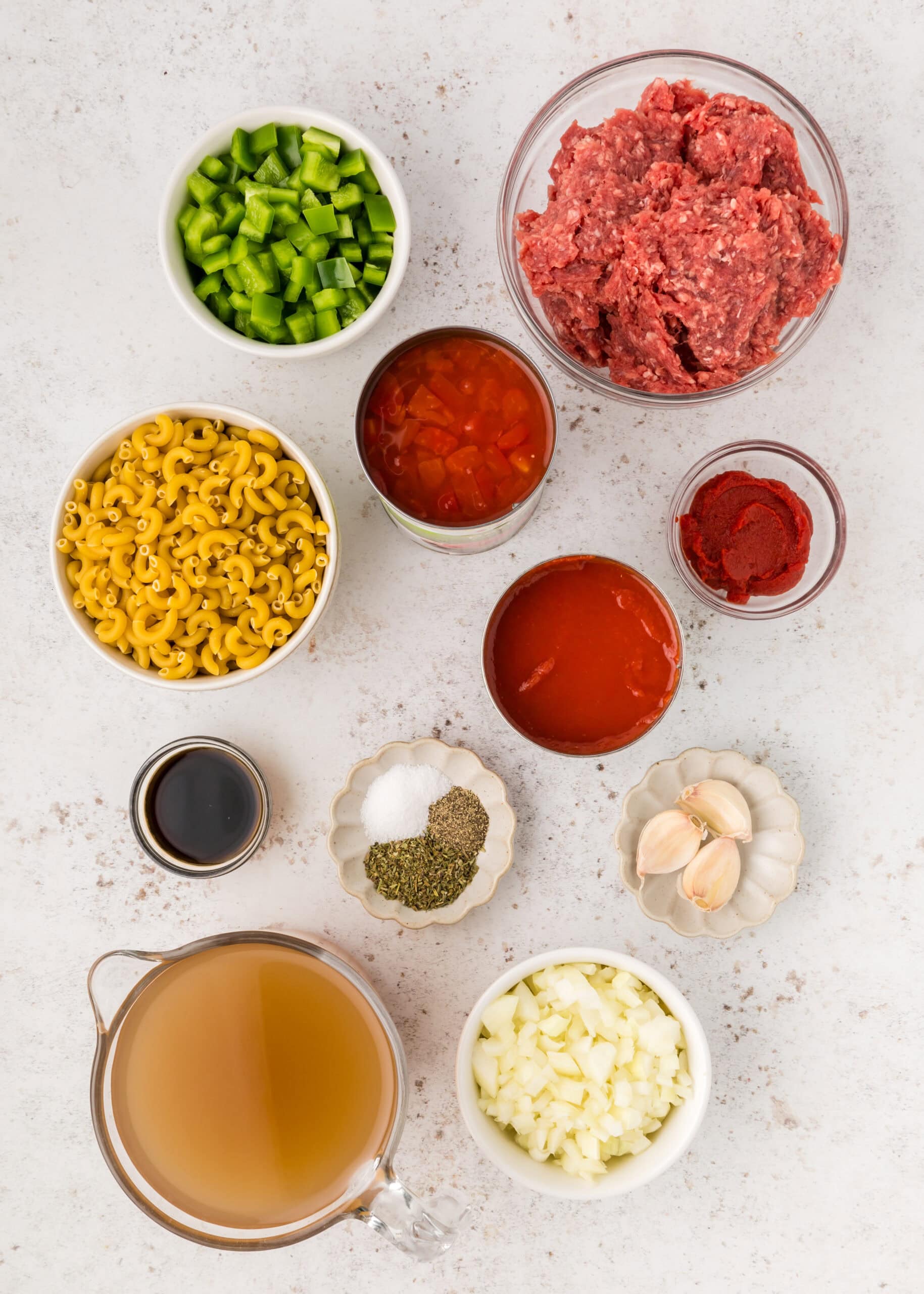Overhead view of ingredients needed to make goulash in separate bowls. 
