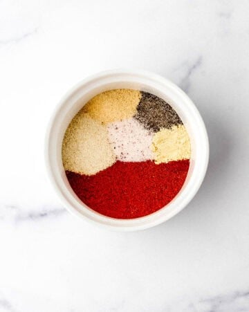 Spices added to white bowl on marble surface.