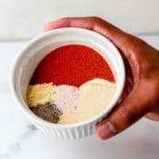 Hand holding white bowl with spices in it.