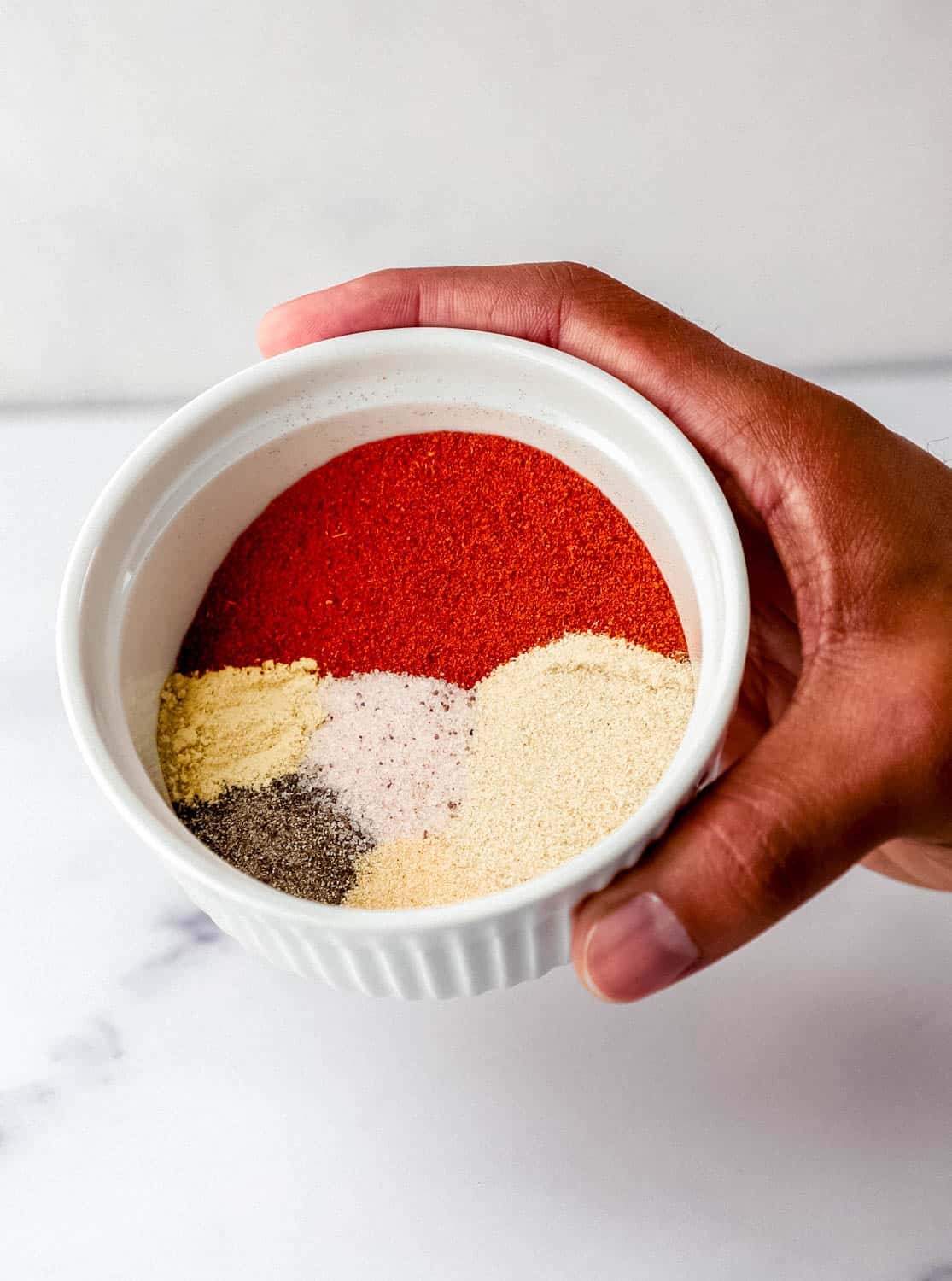 Hand holding small white bowl with spices in it.
