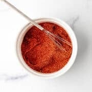Overhead view of seasoning in white bowl with small whisk.