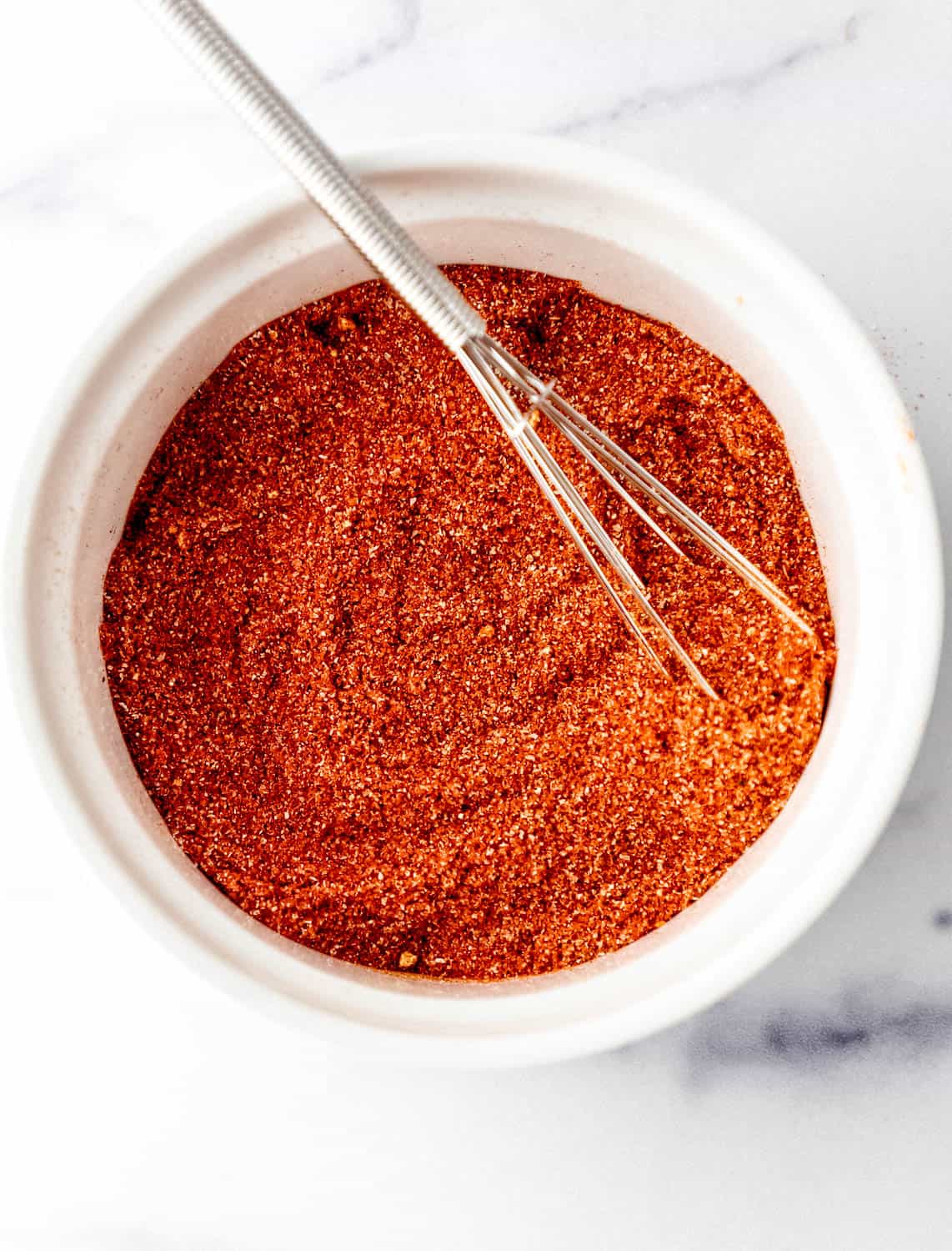 Overhead view of seasoning blend in white bowl with small whisk.