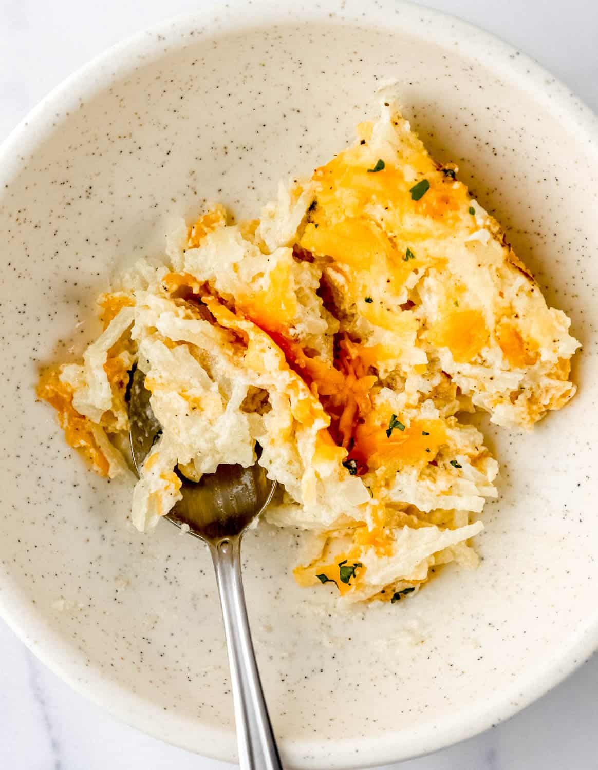 Close up view of serving of casserole in bowl with spoon in it.