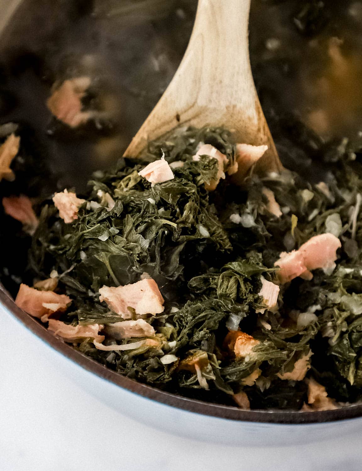 Close up view of cooked mustard greens in dutch oven with wooden spoon.
