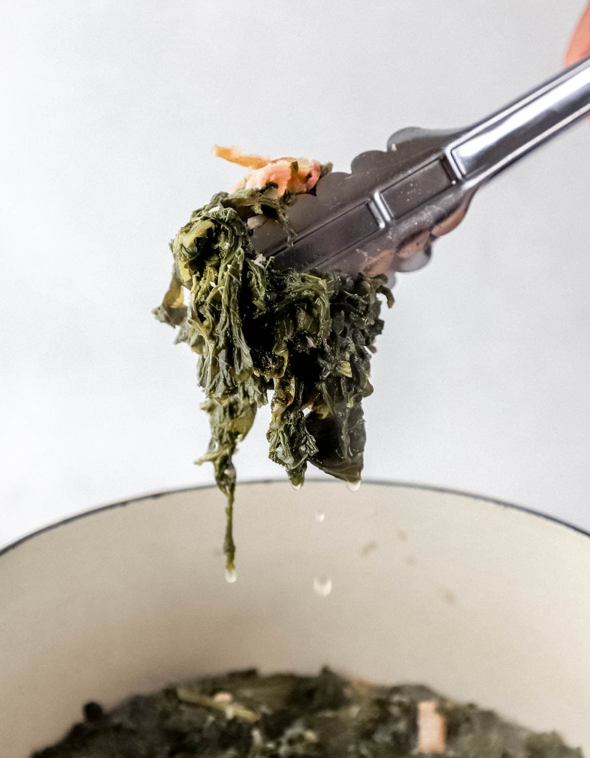 Close up view of hand holding tongs over pot of greens.