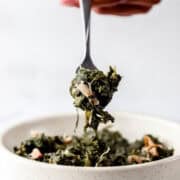 Hand holding fork full of greens over bowl.