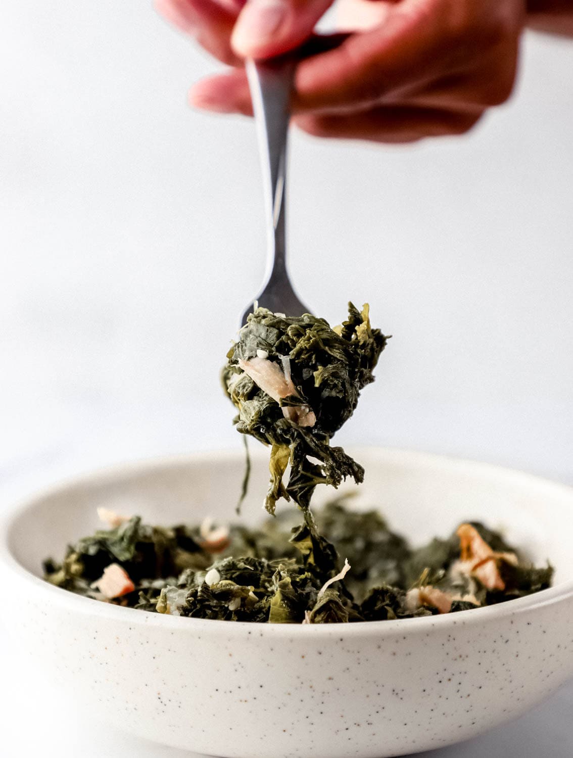 Hand holding fork full of greens over bowl.