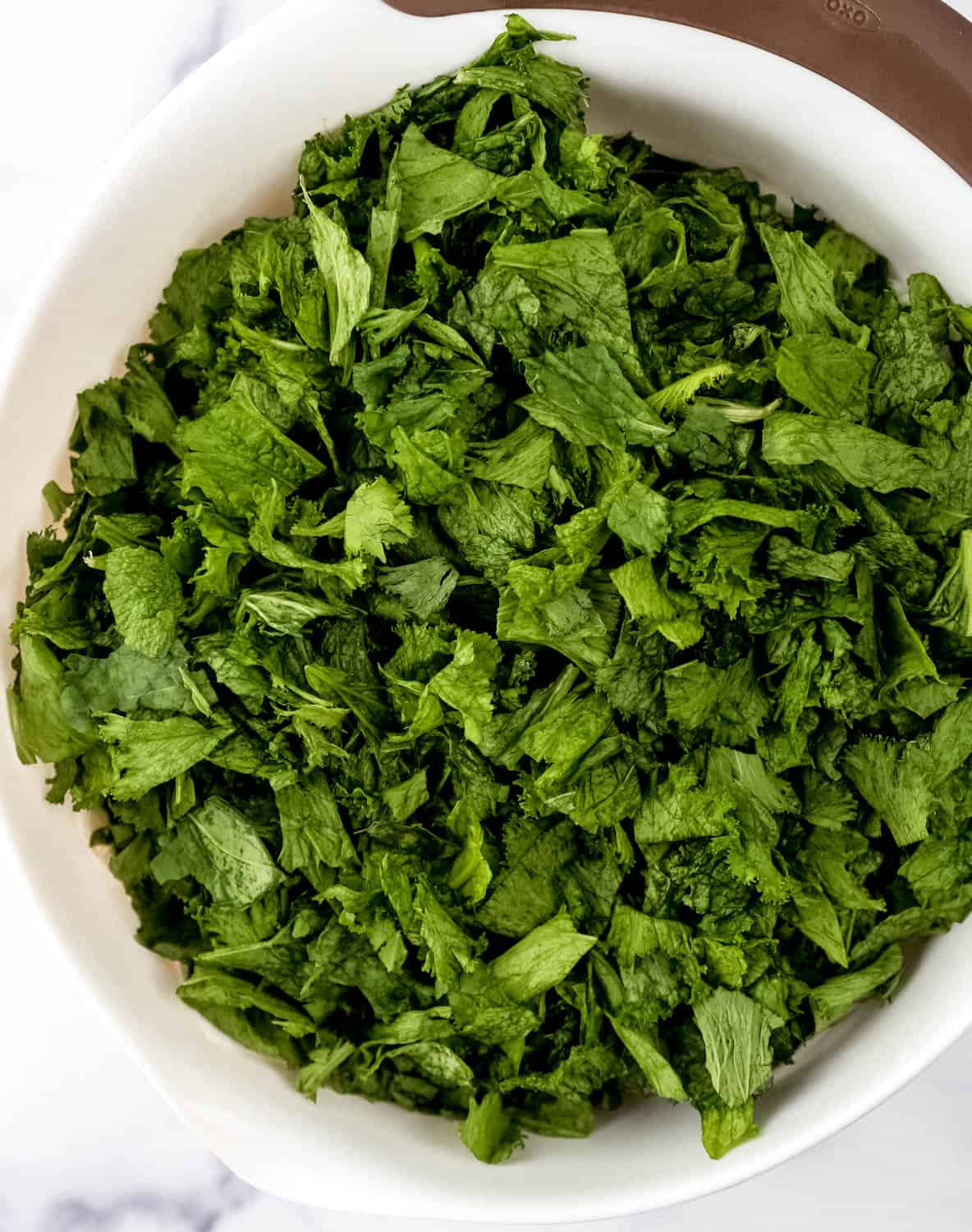 Overhead view of fresh mustard green in large white mixing bowl.