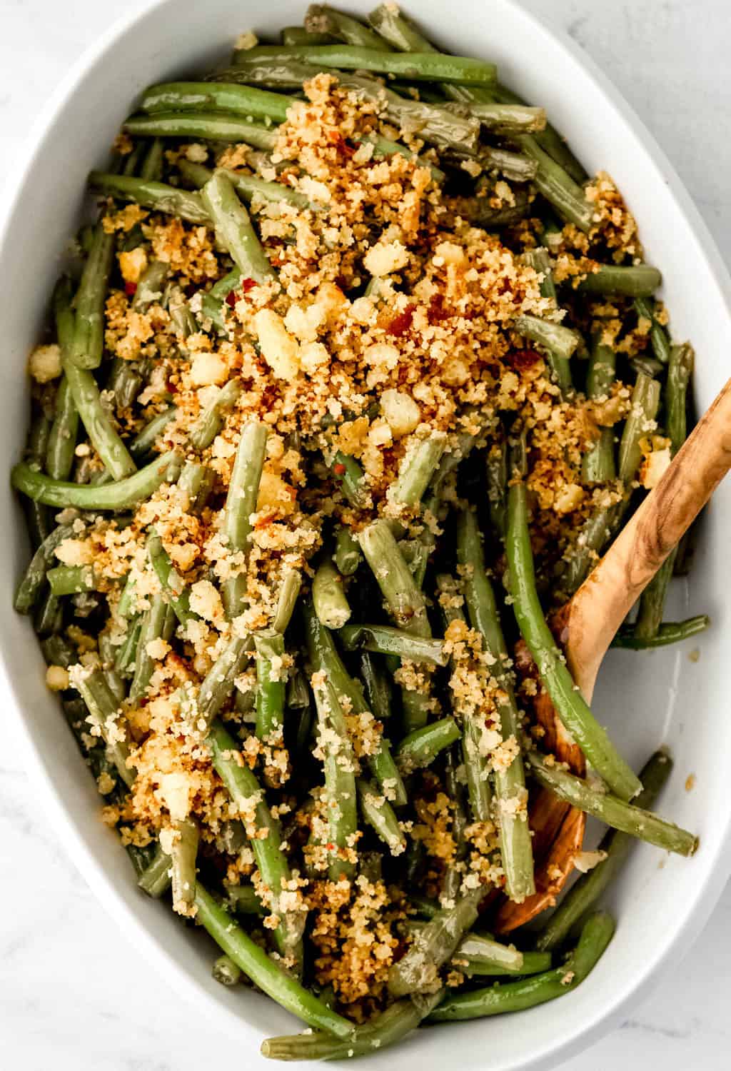 Overhead view of finished green beans in white dish with wooden spoon.