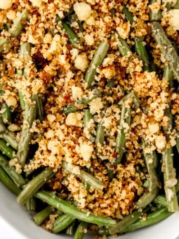 Close up view of green beans topped with cornbread in white dish.