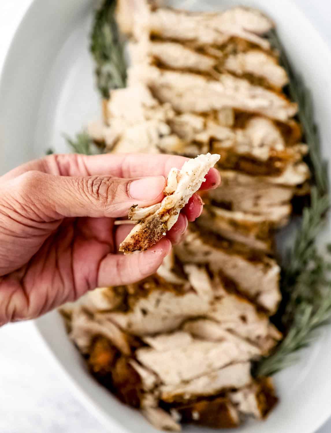 Close up view of hand holding piece of finished turkey breast. 