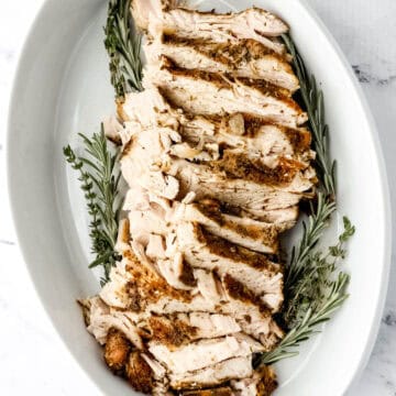 Overhead view of sliced turkey and herbs in white baking dish.