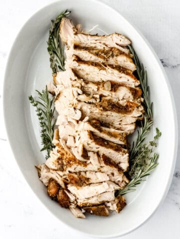 Overhead view of sliced turkey and herbs in white baking dish.