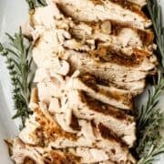 Overhead view of sliced turkey in white baking dish with herbs on pin with text overlay.