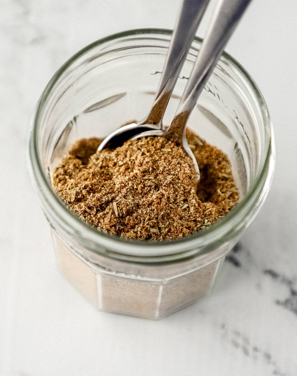 Seasoning added to a glass jar with two spoons. 