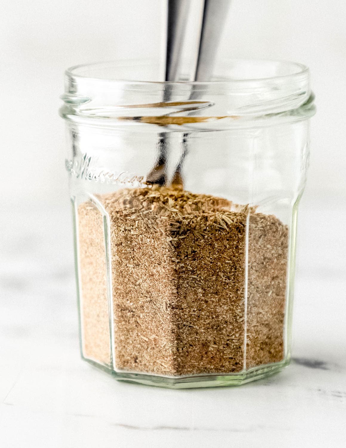 Close up side view of jar of seasoning with spoons in it. 
