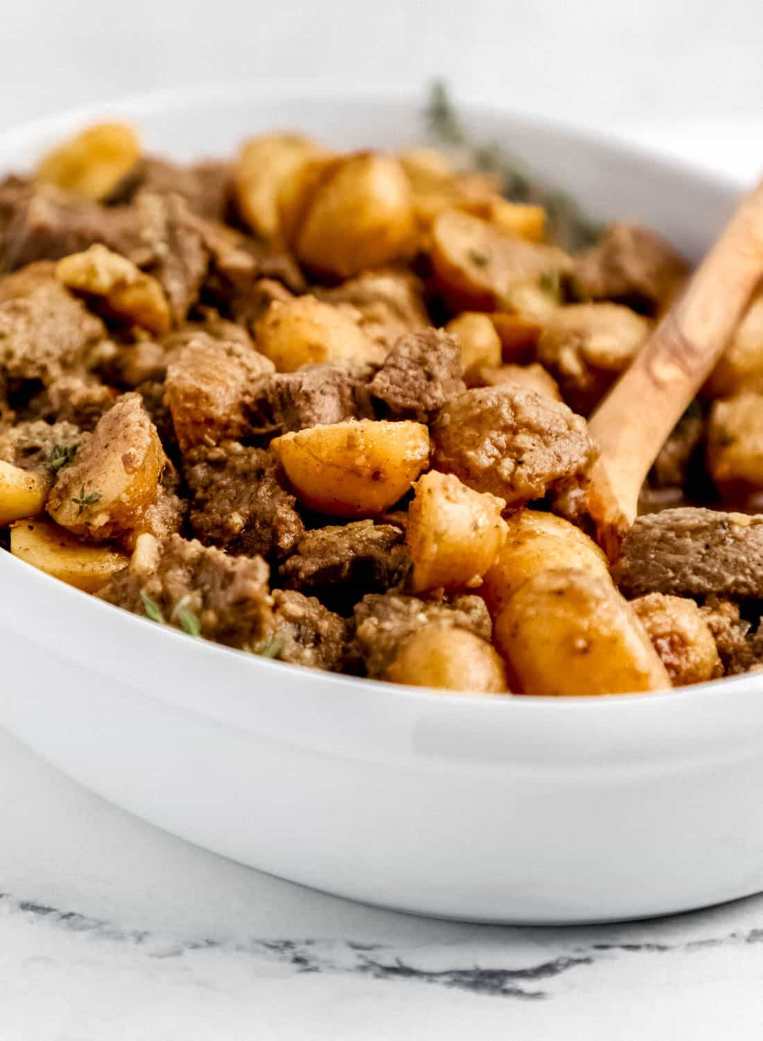 Close up side view of finished steak bites in white dish with wooden spoon in it.