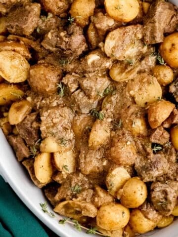 Close up overhead view of finished steak and potatoes in white serving dish.