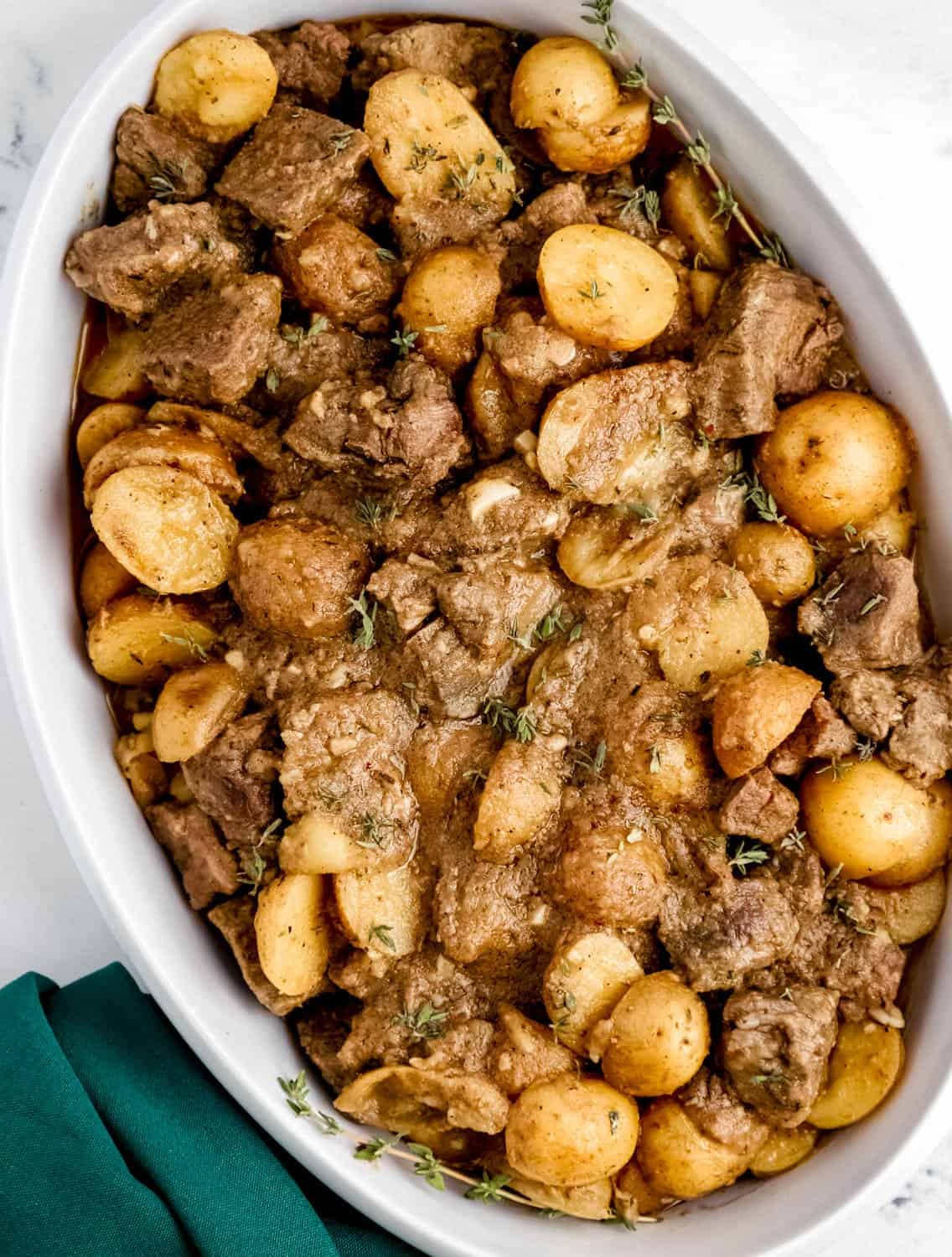 Overhead view of finished steak and potatoes in white serving dish by cloth napkin.