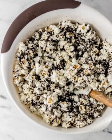Melted chocolate and processed cookies combined with popcorn in bowl with spatula.