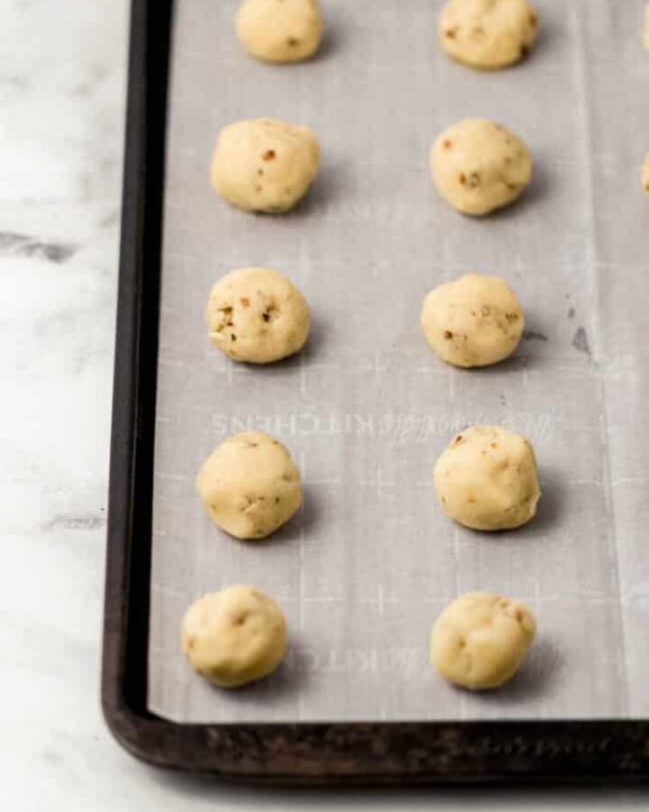 Close up view of cookie dough balls on parchment lined sheet pan.